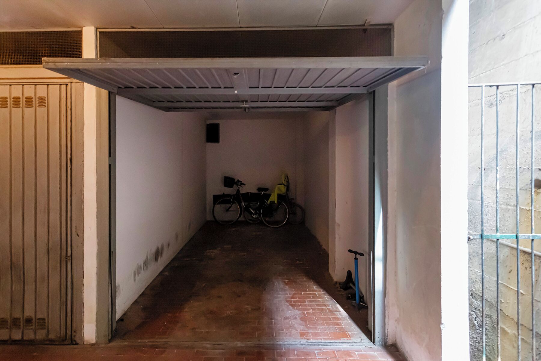 Um corredor estreito com chão de tijolos, uma bicicleta e um patinete.