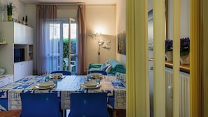 A dining area with a table set for four, chairs, a sofa, a lamp, and a view through a window with curtains. - Relax Apartment with Parking by Wonderful Italy (Santa Margherita Ligure)