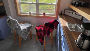 A kitchen with a window, two chairs, a coffee maker, and a sign that says "Rise & Shine". - The Moose, Twillingate Island (Crow Head)