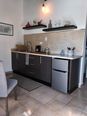 A modern kitchen with a built-in sink, dark cabinetry, a stainless steel refrigerator, and a brick backsplash.
