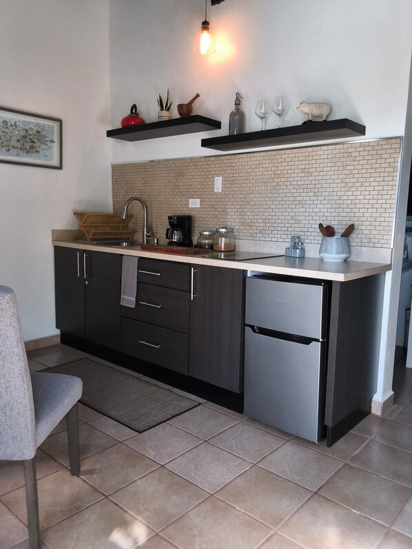 A modern kitchen with a built-in sink, dark cabinetry, a stainless steel refrigerator, and a brick backsplash. - Cheo Villa, Justice Farm (Corozal)