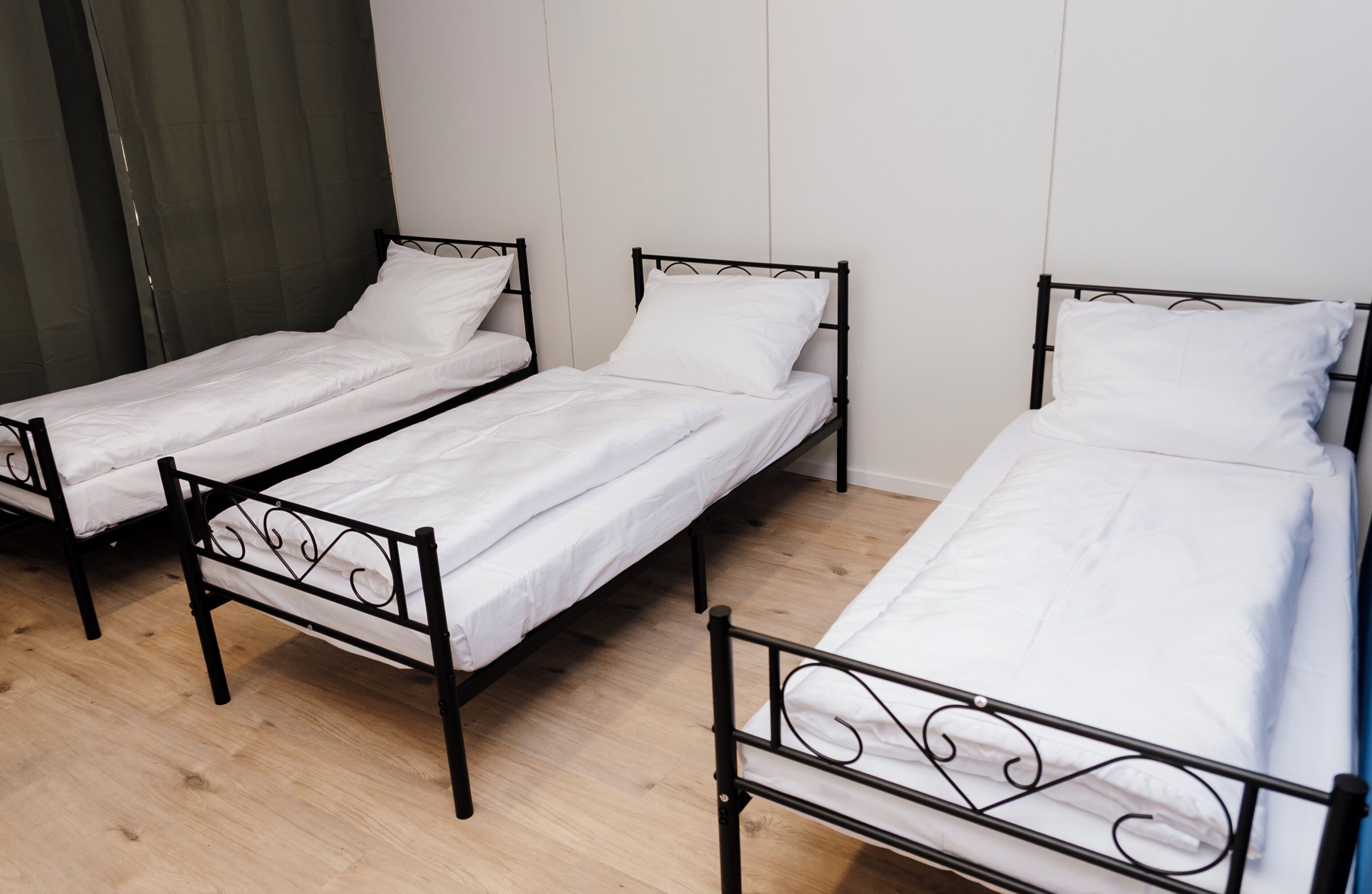 Three single beds with black metal frames and white bedding in a room with wooden flooring.