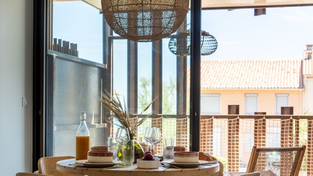 A dining table with chairs, a bottle of drink, and glassware set for a meal. - La Maison de la Plage - Solea 3 Personnes (Mauguio)