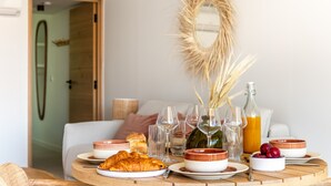 A breakfast setting with croissants, fruit, and beverages on a wooden table, with a mirror and decorative elements in the background. - La Maison de la Plage - Solea 3 Personnes (Mauguio)