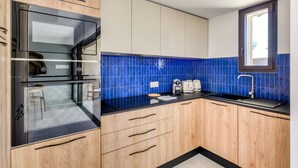 A modern kitchen with wooden cabinets, a black countertop, a built-in oven, and a window above the sink. - La Maison de la Plage - Alma 4 Personnes (Mauguio)