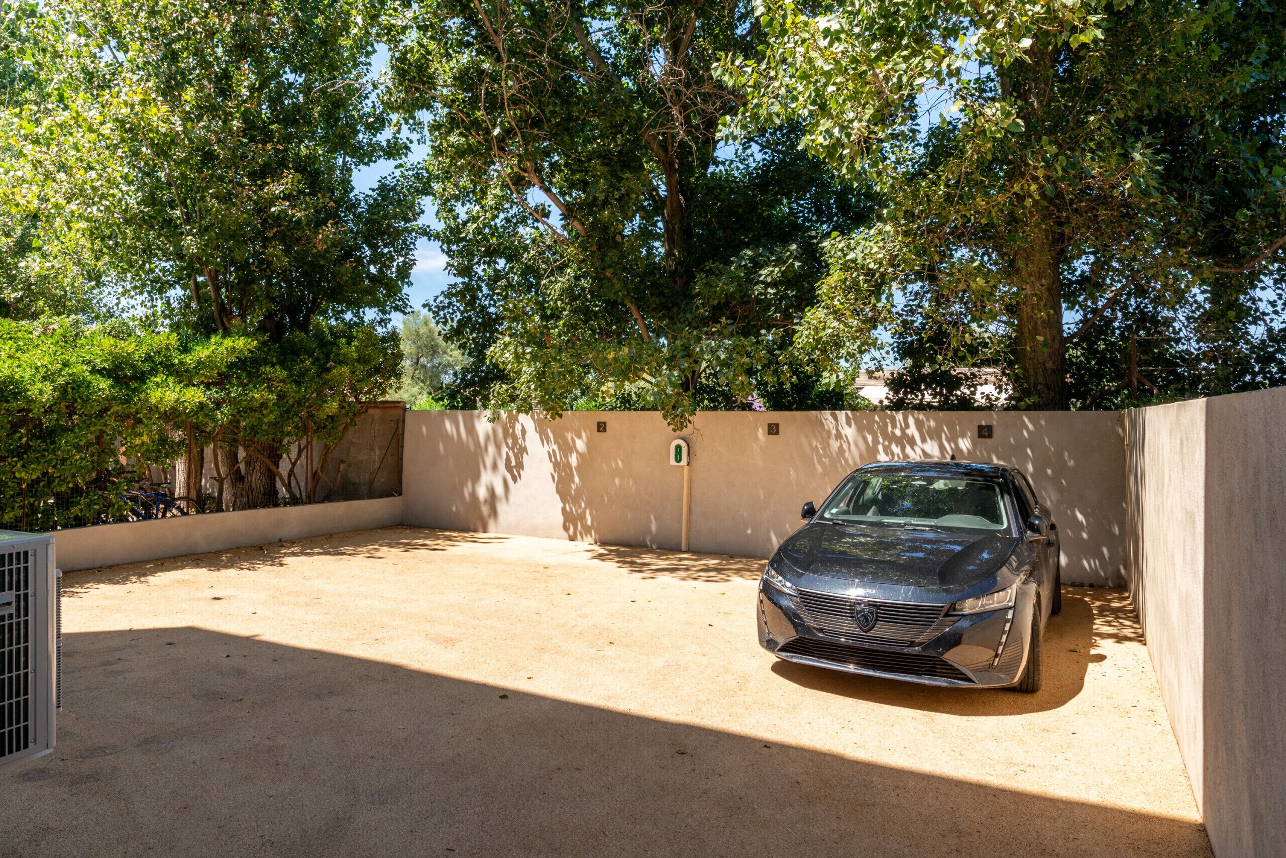 Un coche aparcado en un espacio cubierto al aire libre, con un muro de hormigón y árboles de fondo.