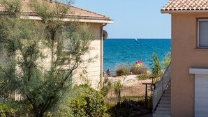 A coastal view with a sandy beach, a sailboat, and a person walking. - La Maison de la Plage - Edena 4 Personnes (Mauguio)