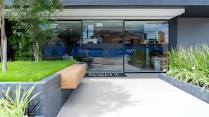 A modern building entrance with glass doors, a bench, and a pathway leading to the entrance. - Emunah Suites Ponta de Campina (Cabedelo)