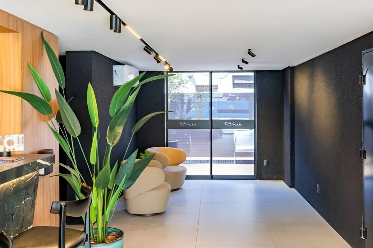A modern interior with a reception desk, a large potted plant, and a seating area with a glass door leading outside.