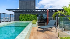 A rooftop pool with a lounge chair, a glass railing, and a modern building in the background. - Emunah Suites Ponta de Campina (Cabedelo)
