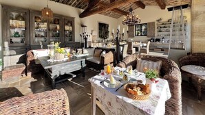 A rustic dining area with wooden beams, wicker furniture, and a variety of table settings. - Villa Hautvallon (Gordes)