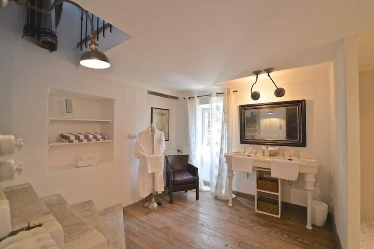 A bathroom with a wooden floor, a white sink, a mirror, and a chair.