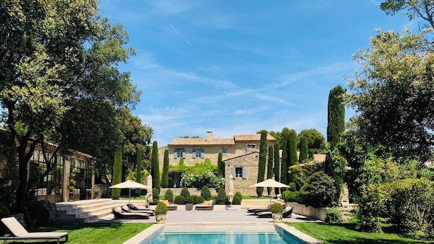 A swimming pool with lounge chairs and umbrellas, surrounded by well-maintained greenery and a stone building in the background. - Villa Hautvallon (Gordes)