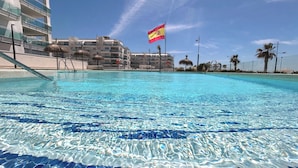 Une piscine aux eaux cristallines, un drapeau, des bâtiments modernes et des palmiers.
