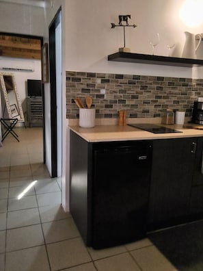 A modern kitchen with a black dishwasher, a tiled backsplash, and a small countertop with a coffee maker.