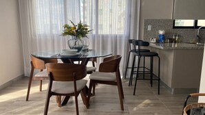 A modern kitchen with a dining area, featuring a round glass table, wooden chairs, and a kitchen counter with appliances. - Amazing apartment near Blue Mall with pool in Regatta Living YellowKey (Santo Domingo)