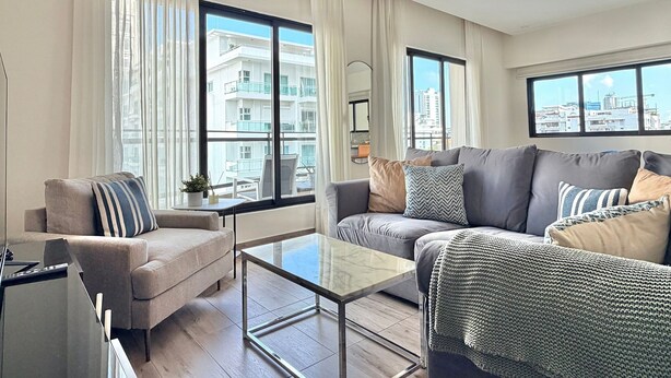 A modern living room with two sofas, a glass coffee table, and large windows offering city views. - Amazing apartment near Blue Mall with pool in Regatta Living YellowKey (Santo Domingo)