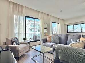 A modern living room with two sofas, a glass coffee table, and large windows offering city views. - Amazing apartment near Blue Mall with pool in Regatta Living YellowKey (Santo Domingo)