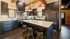Una cucina moderna con pensili in legno scuro, una grande isola con sgabelli, elettrodomestici in acciaio inossidabile e luci a sospensione.