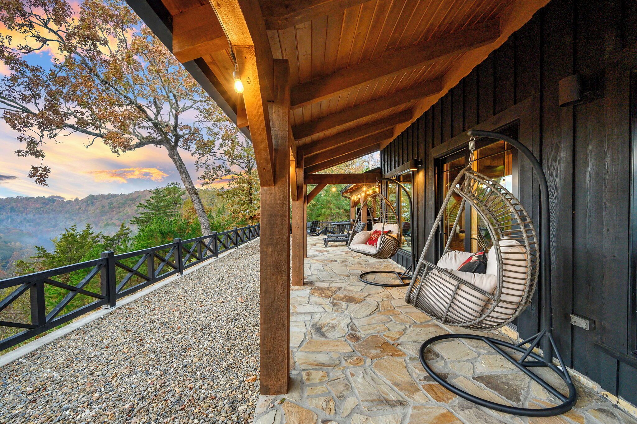A covered outdoor area with stone flooring, wooden beams, and a view of a mountainous landscape.