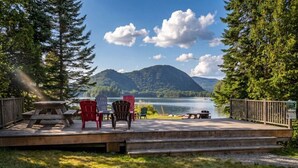 A deck with chairs, a picnic table, and a view of a lake and mountains.
