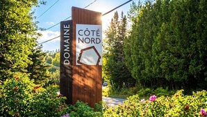 A wooden signpost with 'DOMAINE' and 'CÔTE NORD' text, surrounded by lush greenery and flowers.
