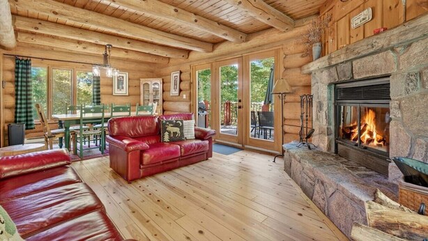 A log cabin interior with a fireplace, wooden floors, a red leather sofa, and a dining area.