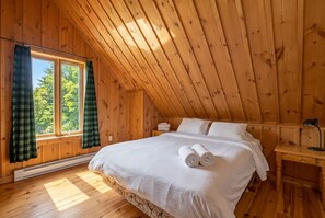 Una habitación de madera con una cama, una mesita de noche y una ventana con cortinas.