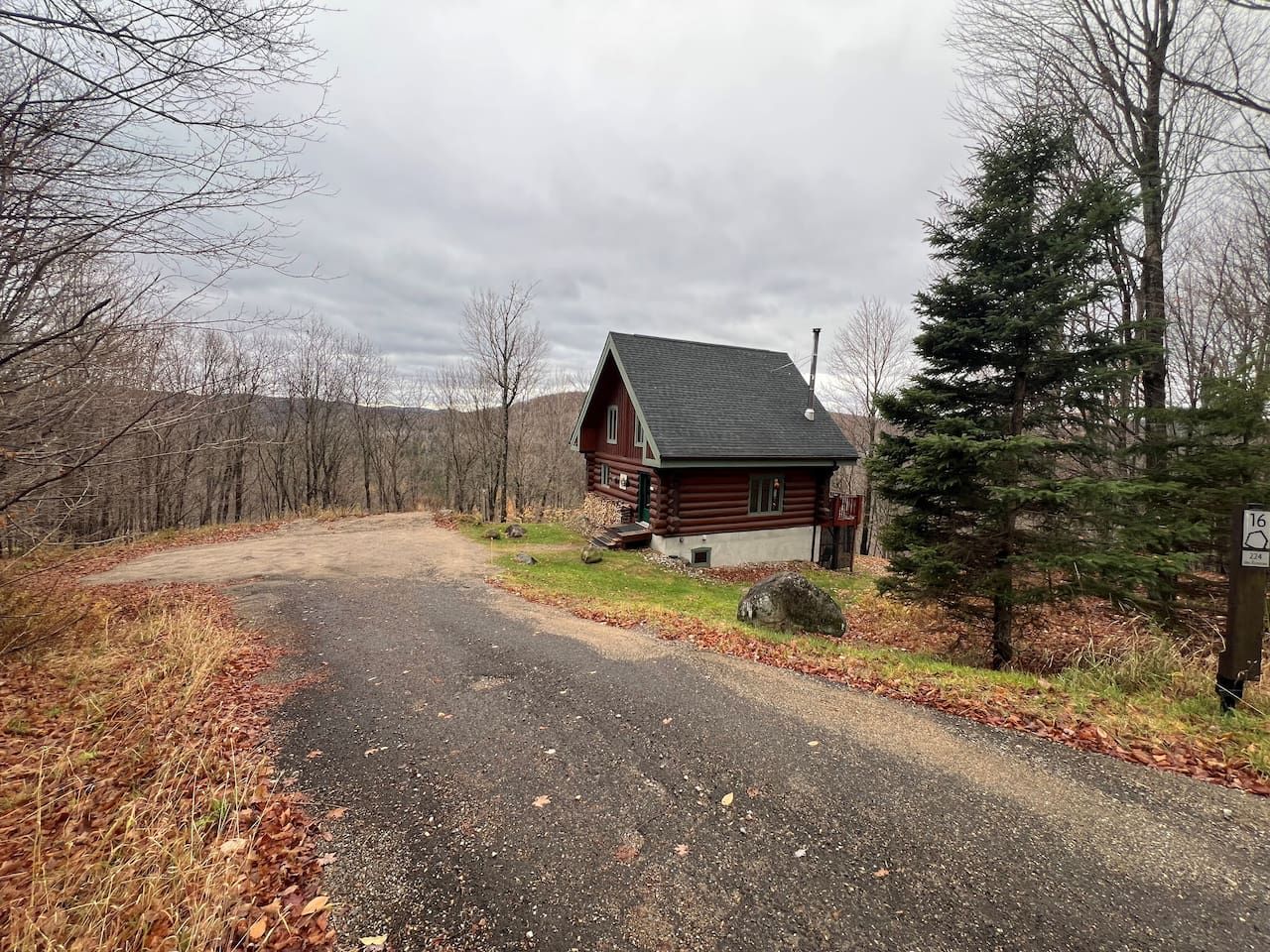 Une cabane avec une allée en gravier, entourée d’arbres et sous un ciel nuageux.