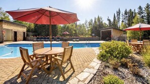 A pool area with a table and chairs, surrounded by a brick patio and greenery.