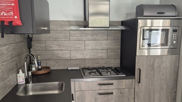 A modern kitchen with a gas stove, stainless steel oven, and a built-in microwave. - Bungalowpark Simpelveld - Alpha 95 (Simpelveld)