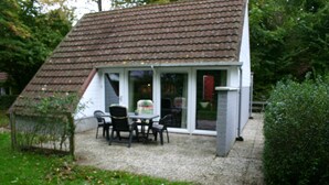 A small house with a tiled roof, a patio with a table and chairs, and a gravel driveway. - Bungalowpark Simpelveld - Alpha 95 (Simpelveld)