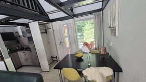 A dining area with a table, chairs, and a vase of flowers. There is a kitchen visible in the background. - Bungalowpark Simpelveld - Alpha 95 (Simpelveld)
