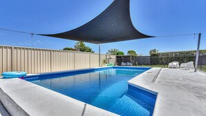 A swimming pool with a shade sail, a fence, and outdoor furniture. - Helena Grand Estate Hunter Valley (Ellalong)