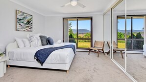 A bedroom with a bed, a ceiling fan, a large window, and a chair. - Helena Grand Estate Hunter Valley (Ellalong)