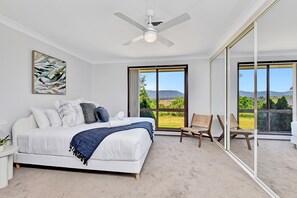 A bedroom with a bed, a ceiling fan, a large window, and a chair. - Helena Grand Estate Hunter Valley (Ellalong)