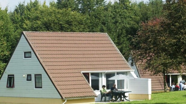 Un petit bâtiment de forme triangulaire, doté d’un toit en pente, d’un porche avec une table et des chaises, et d’une pelouse verdoyante.