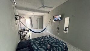 A room with a bed, a desk, a chair, a hammock, a television, and a mirror. - Private rooms with climate control, fan and internet (Tulum)