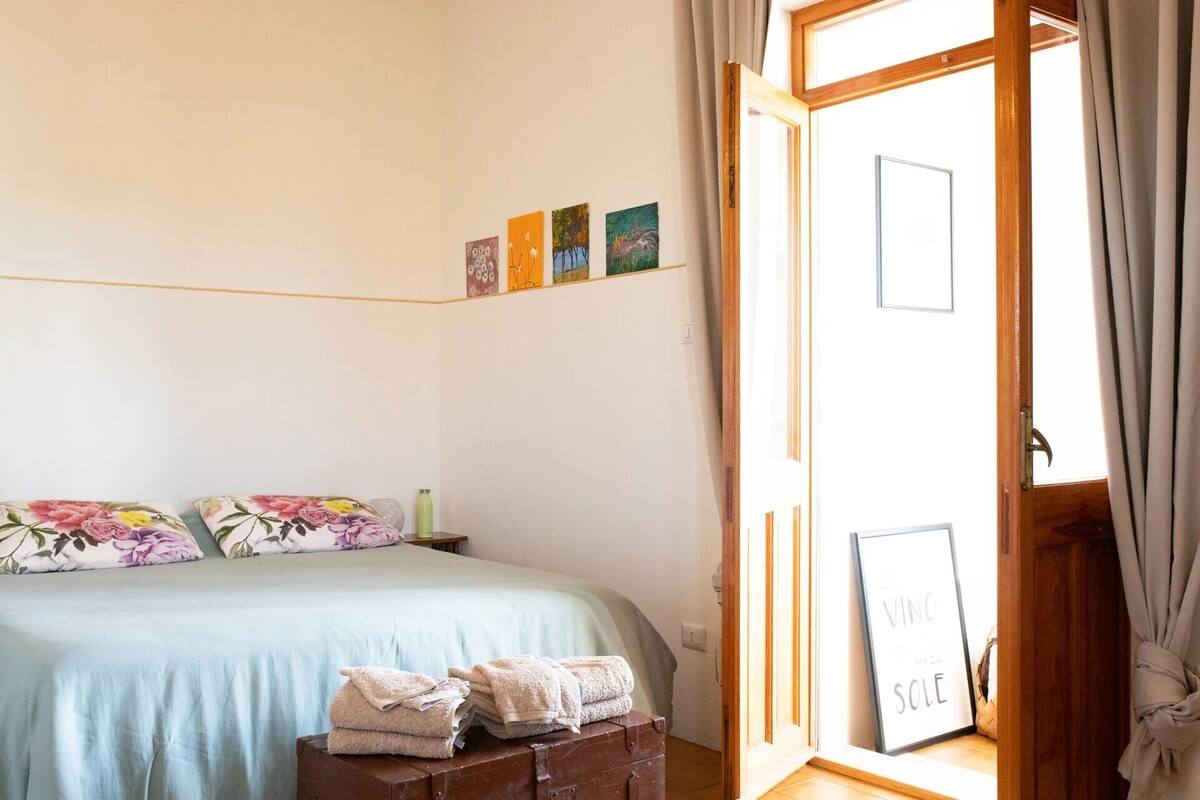 A bedroom with a bed, pillows, a suitcase, and a door with a sign.