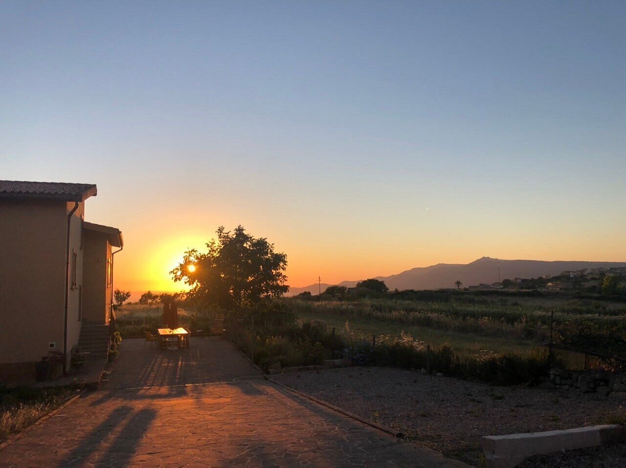 Paisagem rural com uma casa, uma árvore e um pôr do sol.