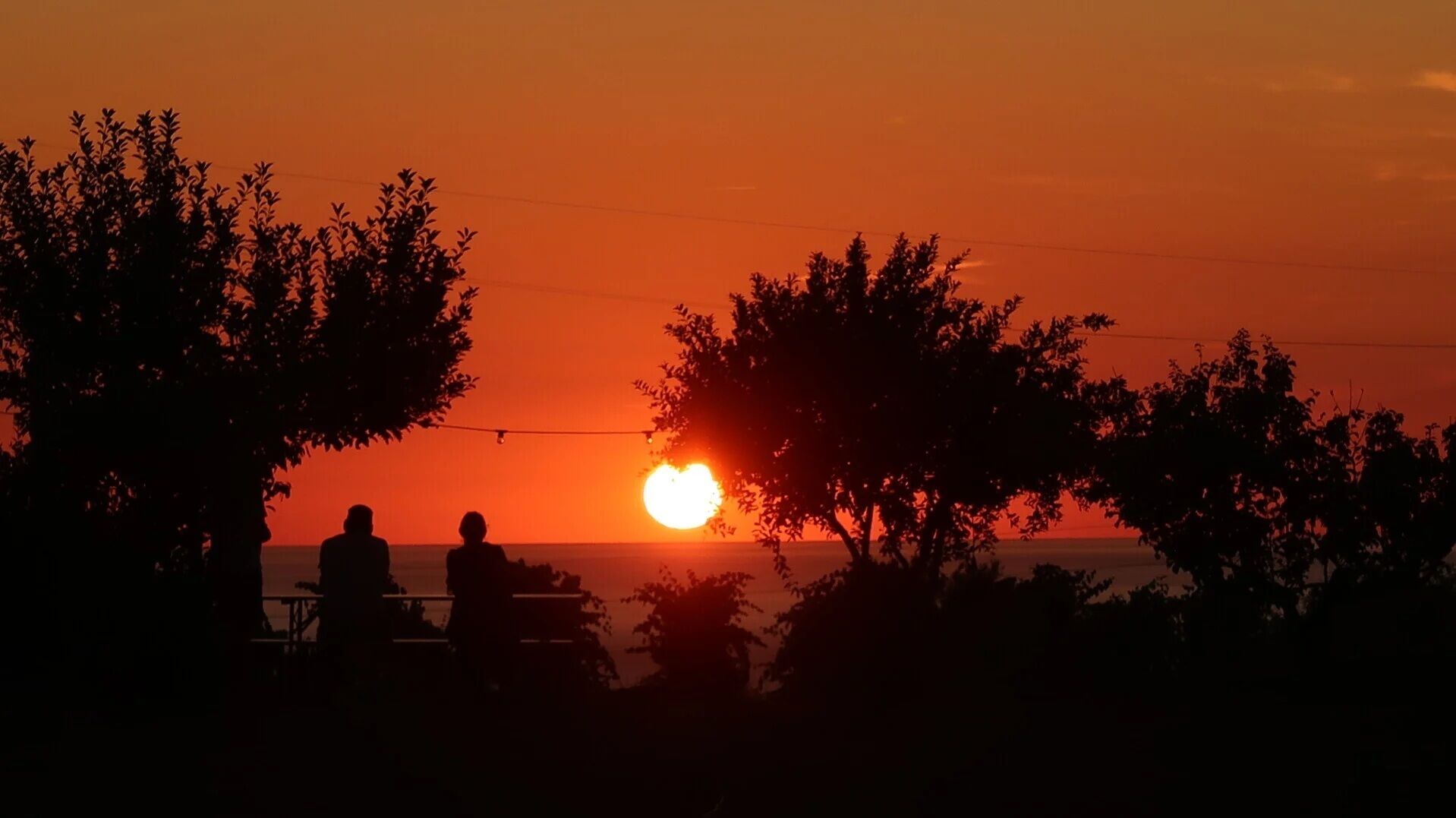 Un atardecer con siluetas de dos personas y árboles en primer plano.