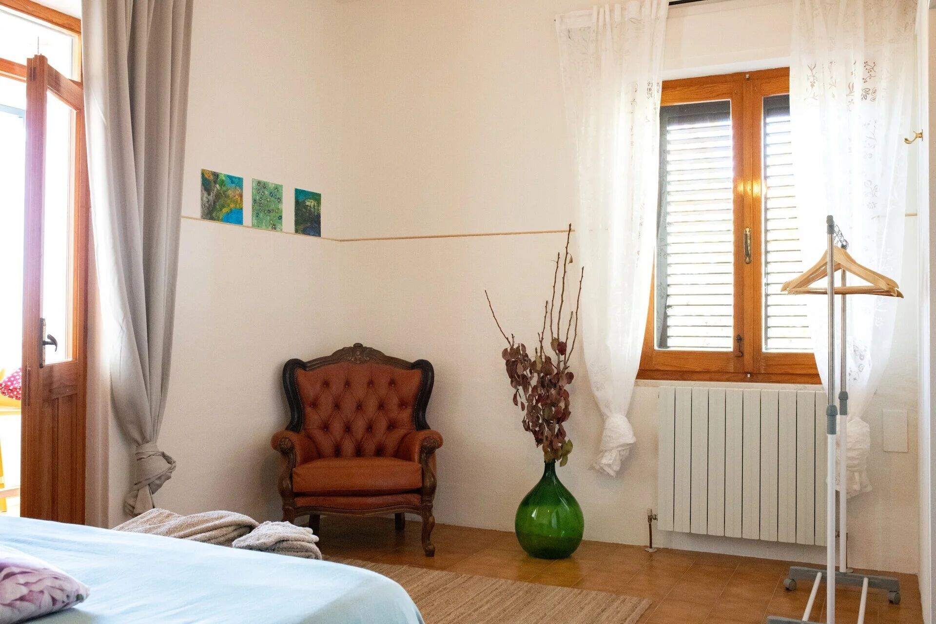 A bedroom with a bed, a chair, a radiator, and a window with curtains.