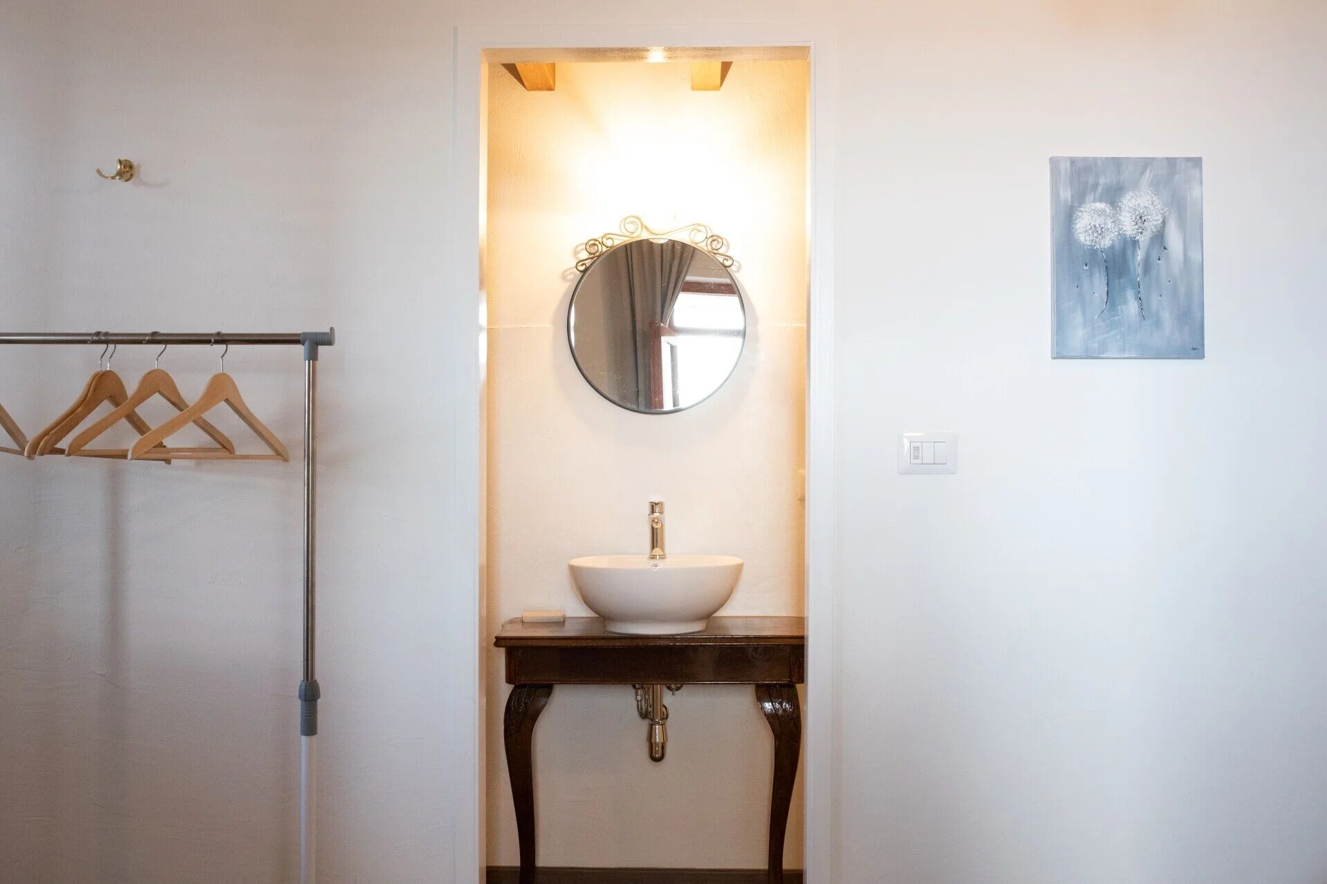 Une salle de bain avec un miroir rond, un lavabo blanc et un porte-manteau en bois.