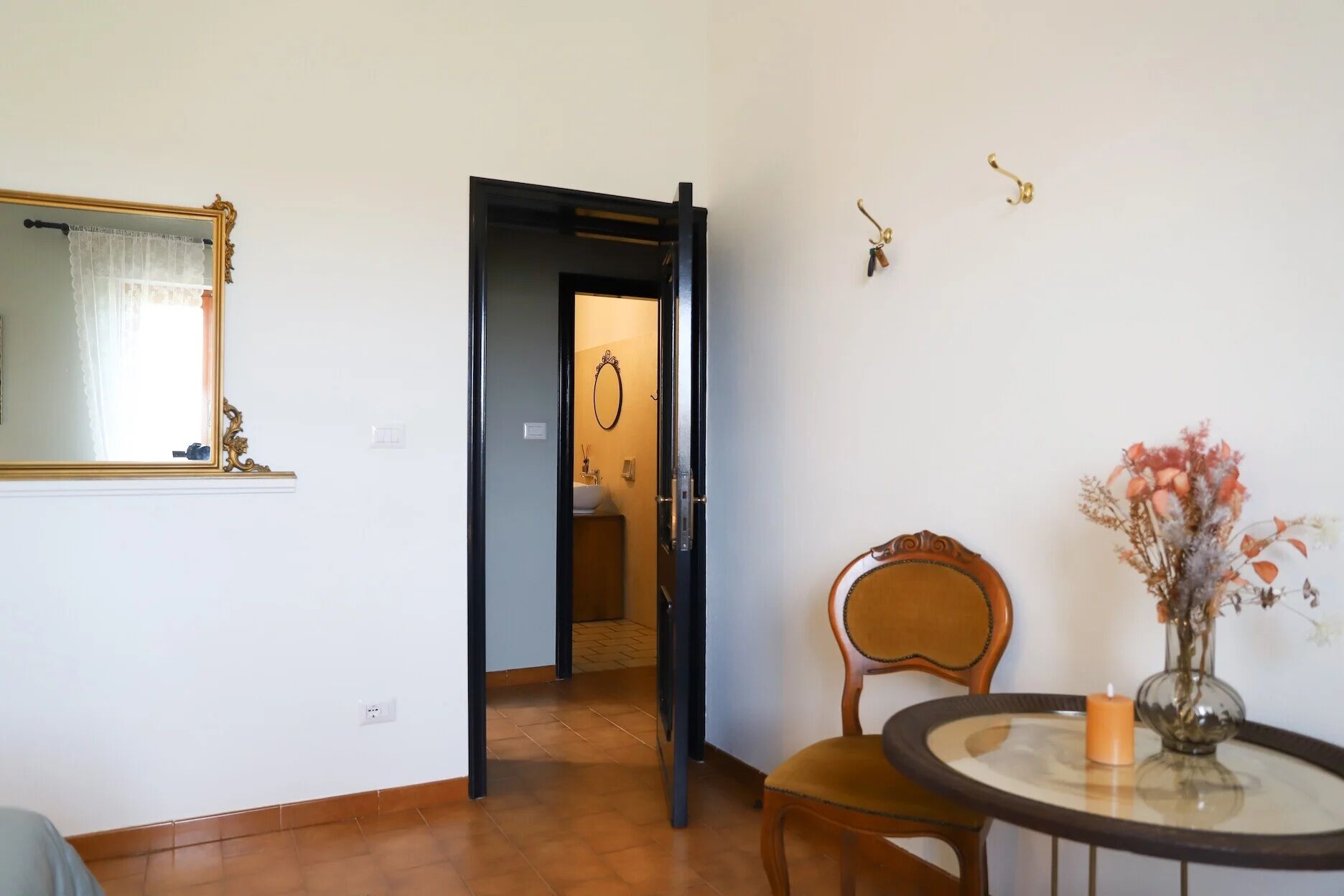 A room with a wooden chair, a small table with a candle, and a mirror with a gold frame.