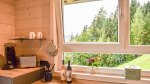 A kitchen with wooden cabinets, a window with a view of greenery, a toaster, a coffee maker, and a vase with flowers. - Holiday Home 'Panoramahisli 3' with Mountain View, Balcony and Air Conditioning (Fischerbach)