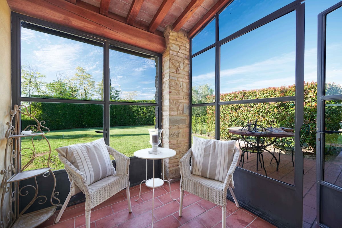 Une terrasse avec des chaises en osier, une petite table et une vue sur un jardin.