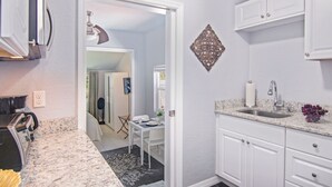 Une cuisine moderne avec des meubles blancs, un plan de travail en granit et un coin repas visible à travers une porte ouverte.