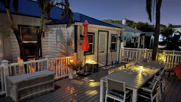 Une terrasse avec une table et des chaises, un petit bâtiment avec un toit bleu et une clôture blanche.