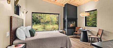 A modern bedroom with a large bed, a fireplace, and a view of the outdoors.