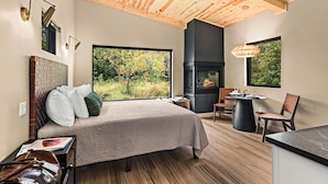 A modern bedroom with a large bed, a fireplace, and a view of the outdoors. - Private Sauna + Fireplace · Wildernest Cabins #3 (Duluth)